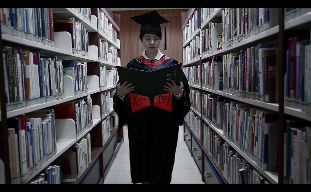 万青《杀死那只同性恋》影片画面：身穿学士服的学生在图书馆朗读。